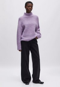 Hellblauer, gerippter Strickpullover mit Rollkragen und überschnittenen Schultern, kombiniert mit schwarzen, weit geschnittenen Hosen und schwarzen Schuhen.