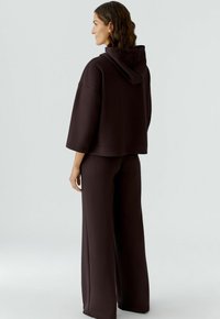 Brauner oversized Kapuzenpullover mit Kängurutasche und Kapuze, kombiniert mit passenden weiten Hosen, aus einem weichen Stoff gefertigt.