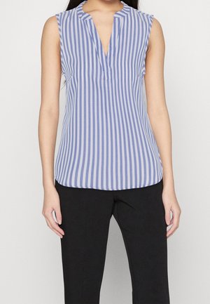 Ärmellose blau-weiße Bluse mit vertikalen Streifen und V-Ausschnitt, getragen mit schwarzen Hosen an einer Person vor einfarbigem Hintergrund.