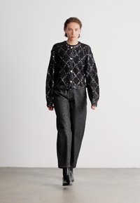 Casaco preto com lantejoulas, em padrão de diamante acolchoado, combinado com calças retas de tom cinza escuro texturizado e botas de tornozelo pretas.