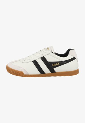 White leather sneakers with black stripes, gold logo, and textured gum rubber sole. Lace-up design with a smooth finish and padded collar.