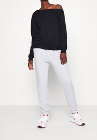 Sudadera negra sin hombros, pantalones de chándal grises y zapatillas blancas con detalles en rojo. Tela suave, ajuste holgado y puños acanalados.