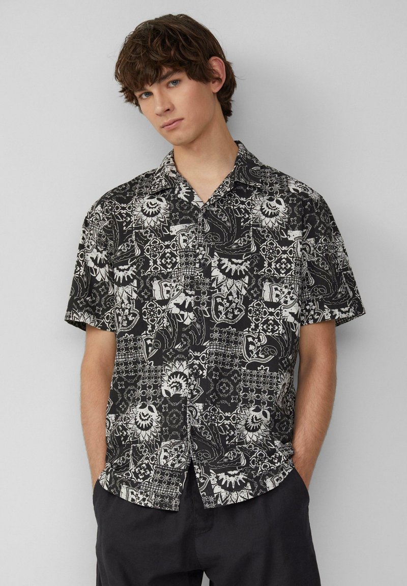 Korte mouwen zwart shirt met witte ingewikkelde bloemen- en paisleypatronen. Lichtgewicht stof, relaxte pasvorm en een button-down kraagontwerp.