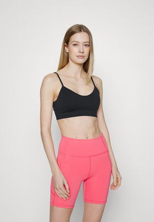 Bralette de desporto preto com alças finas, combinado com calções cor-de-rosa de cintura alta. Ambos são feitos de um tecido elástico com costuras para estrutura.