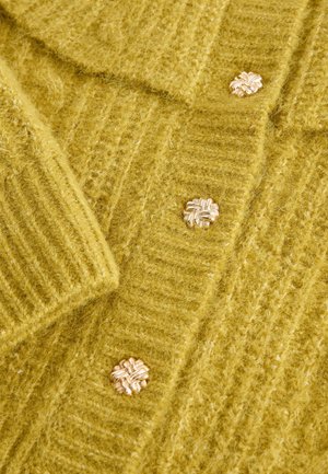 Knit cardigan in soft, fluffy yellow material, featuring a textured ribbed design and gold-tone floral buttons.