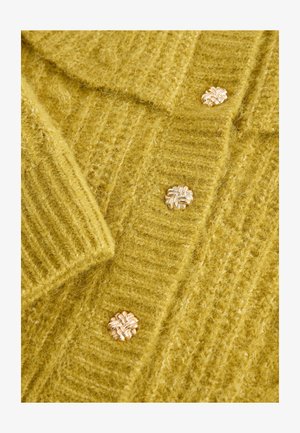 Cardigan lavorato a maglia in morbido e soffice materiale giallo, caratterizzato da un design a coste testurizzate e bottoni floreali color oro.