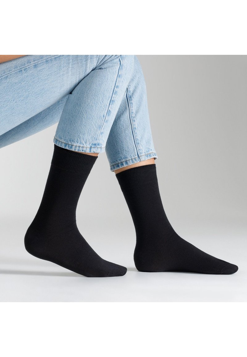 Schwarze Knöchelsocken aus weichem Material, mit einem gerippten Bündchen, glatter Textur und klassischer Passform, kombiniert mit hellblauen Jeans.