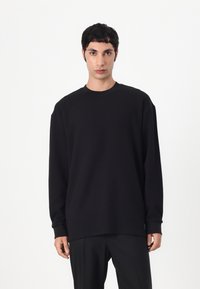 Sweatshirt noir à manches longues avec un col rond, des poignets côtelés et une coupe décontractée. Fabriqué en tissu doux avec une texture lisse.