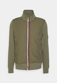 Oliwkowa zielona kurtka z wysokim kołnierzem, przednim zamkiem błyskawicznym i teksturowaną tkaniną. Z elementem kontrastowego białego i czerwonego zamka. Długie rękawy.