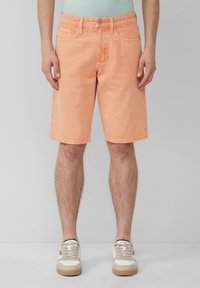 Shorts en denim couleur pêche avec une coupe droite, cinq poches et des coutures contrastées, associés à des baskets beiges.