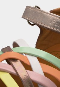 Κοντινή εικόνα πολύχρωμων λουριών δερμάτινων σανδαλιών σε παστέλ αποχρώσεις με μεταλλικό λουρί στον αστράγαλο και καφέ πέλμα.