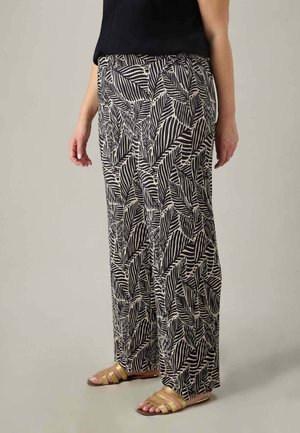 Hochgeschnittene Hosen im schwarz-weißen Blättermuster, gefertigt aus einem glatten, leichten Stoff. Kombiniert mit flachen, metallischen Sandalen.