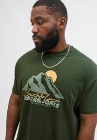 Grünes Baumwoll-T-Shirt mit einem Bergdesign und einer Sonne, akzentuiert mit einem Logo in Weiß und Gelb, runder Ausschnitt, kurze Ärmel.