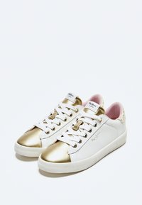 Sneakers bianchi con punta e dettagli dorati lucidi. Presentano una suola bianca, lacci in tessuto e un rivestimento interno rosa chiaro.