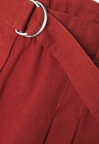 Tissu rouge avec une texture lisse, présentant une ceinture avec une boucle en métal argenté et des plis pour un détail de conception supplémentaire.