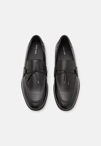 Černé kožené mokasíny s hladkým povrchem, švy jako akcenty a ozdobnou tkaničkou. Zaoblený tvar a měkké stélky pro pohodlí.