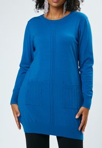 Tunic blu in maglia con maniche lunghe, scollo rotondo, orlo e polsini a coste; presenta due tasche frontali testurizzate con strisce verticali.