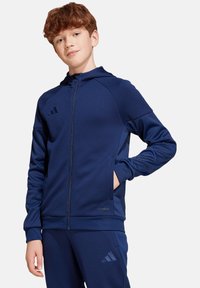 Marineblauwe sportieve zip-up jasje, gemaakt van gladde stof met een capuchon. Beschikt over zijzakken en een reliëflogo op de linkerborst en zoom.