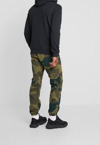 Hooded black sweatshirt paired with green camo pants. Pants feature elastic cuffs and a mix of green and blue patterns. Black athletic shoes with white socks.