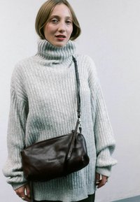 Pull en col roulé gris côtelé, coupe ample ; sac bandoulière en cuir marron avec une finition texturée et une sangle réglable. Fond uni.