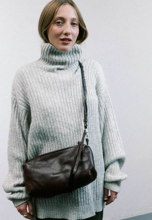 Maglione grigio a coste con colletto a lupetto, vestibilità ampia; borsa a tracolla in pelle marrone con finitura testurizzata e tracolla regolabile. Sfondo uniforme.