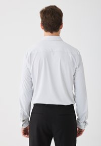 Camicia a maniche lunghe a righe blu chiaro con colletto classico, polsini con bottoni e spacco sulla schiena, abbinata a pantaloni neri.