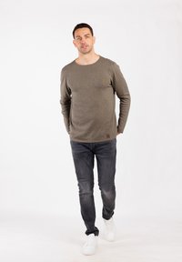 Hellbraunes Langarmshirt mit Rundhalsausschnitt, kombiniert mit dunkelgrauen Jeans und weißen Sneakers. Das Shirt hat eine dezente Textur.