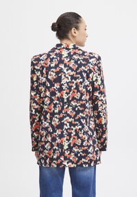 Blazer s květinovým vzorem v námořnické modři, s červenými, oranžovými a zelenými akcenty. Trochu delší, s jedním rozventilem a přiléhavými rukávy.