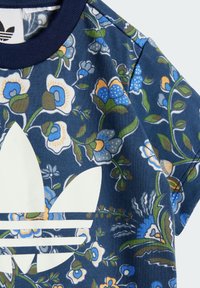 Maglietta a maniche corte blu navy con motivo floreale, caratterizzata da un ampio logo bianco nella parte inferiore. Realizzata in cotone morbido con colletto a girocollo a coste.
