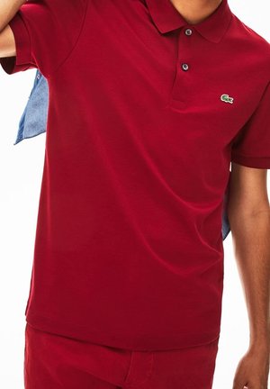 Rotes Baumwoll-Polohemd mit Kragen, kurzen Ärmeln und grünem besticktem Logo auf der Brust; verfügt über einfache Knöpfe und eine glatte Textur.