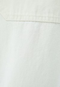 Tela de mezclilla verde claro con un tejido texturizado. Presenta una costura bien terminada y un brillo sutil.