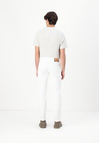 White cotton jeans with five pockets, a straight-leg design, and a brown tag at the back. Worn with a short-sleeve gray t-shirt and footwear.