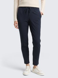 Pantalones tapered en color marino, hechos de una tela suave, con cintura ajustable mediante cordón, bolsillos laterales y puños ceñidos; combinados con zapatillas ligeras.