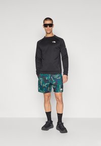 Must have pikad varrukad särk, millel on logo, rohelised kamuflaažilühikesed püksid, mustad spordijalatsid ja prillid. Tekstuuriga kangas, sportlik sobivus ja spordidisain.