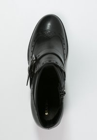Zapato de cuero negro con detalles de brogue, una correa con hebilla y un diseño de punta redonda. El forro interior es de un negro texturizado.