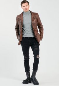 Bruine leren jas met klepzakken, grijze coltrui, versleten zwarte spijkerbroek en zwarte enkellaarsjes met een chunky zool.