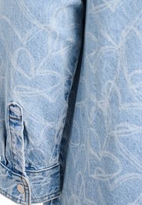 Helehelesinine teksajakk, millel on peen valge lillemuster, nööbitavad varrukad ja tavalised õmblusdetailid õmblustes.