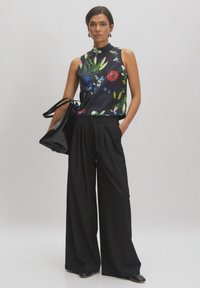 Floral mouwloze blouse met een zwarte achtergrond, gecombineerd met een wijde zwarte broek en een glanzende zwarte handtas. Gladde stoftextuur.