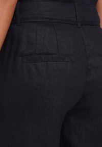 Pantalons en lin noir avec une texture lisse, dotés d'une poche arrière et d'une taille ceinturée pour un ajustement structuré.