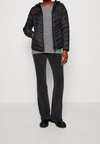 Czarna kurtka puchowa z kapturem, noszona na czarno-białą pasiastą koszulę z długim rękawem, w połączeniu z ciemnoszarymi spódnicami dzwonami i czarnymi botkami.