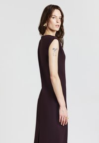 Figurbetontes, ärmelloses Kleid aus tiefburgunderfarbener Stoff, mit einem seitlichen Schlitz, glatter Textur und minimalistischem Design.