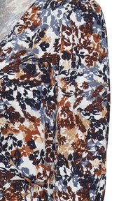 Nahaufnahme eines Stoffes mit mustergemäßem Blumenmotiv in Marineblau, Braun, Beige und Grau auf einem weißen strukturierten Hintergrund.