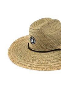 Sombrero de paja con ala ancha, color beige natural, con un parche de logo circular negro y un cordón negro alrededor de la base.