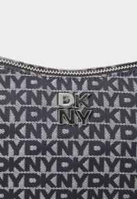 DKNY taske med navy stof og gentagne sorte logo mønstre. Sølv lynlås og metallisk logo akcent på forsiden, tekstureret finish.