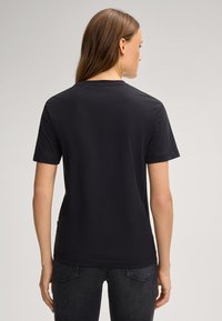 T-shirt noir à manches courtes en tissu léger, avec un col rond simple et une coupe droite, porté avec un jean foncé.