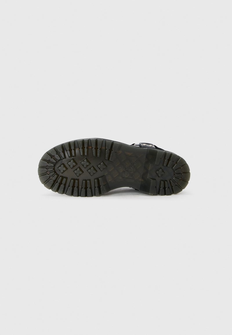 Semelle de chaussure en caoutchouc noir avec des rainures profondes et des motifs angulaires pour une bonne adhérence, présentant des bords texturés et un profil plat.