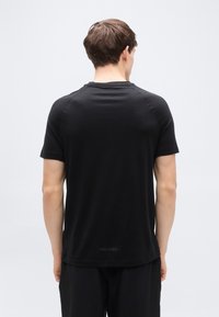 Ανδρικό μαύρο t-shirt με κοντά μανίκια, κατασκευασμένο από λεία ύφασμα, με ριμπ λαιμόκοψη και ίσια ραφή στο τελείωμα με διακριτική λεπτομέρεια λογοτύπου στο πίσω μέρος.