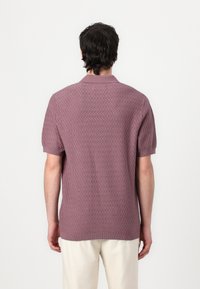 Short-sleeve polo shirt in light purple with a textured zigzag pattern. Ribbed collar and hem, made from a soft knit material.