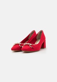 Chaussures en suede rouge à talon bloc avec un bout pointu et une boucle métallique décorative ornée d'embellissements transparents à l'avant.