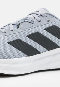 Light gray athletic shoe with textured mesh upper, black three-stripe design, and white rubber sole. Features flat laces and molded accents.